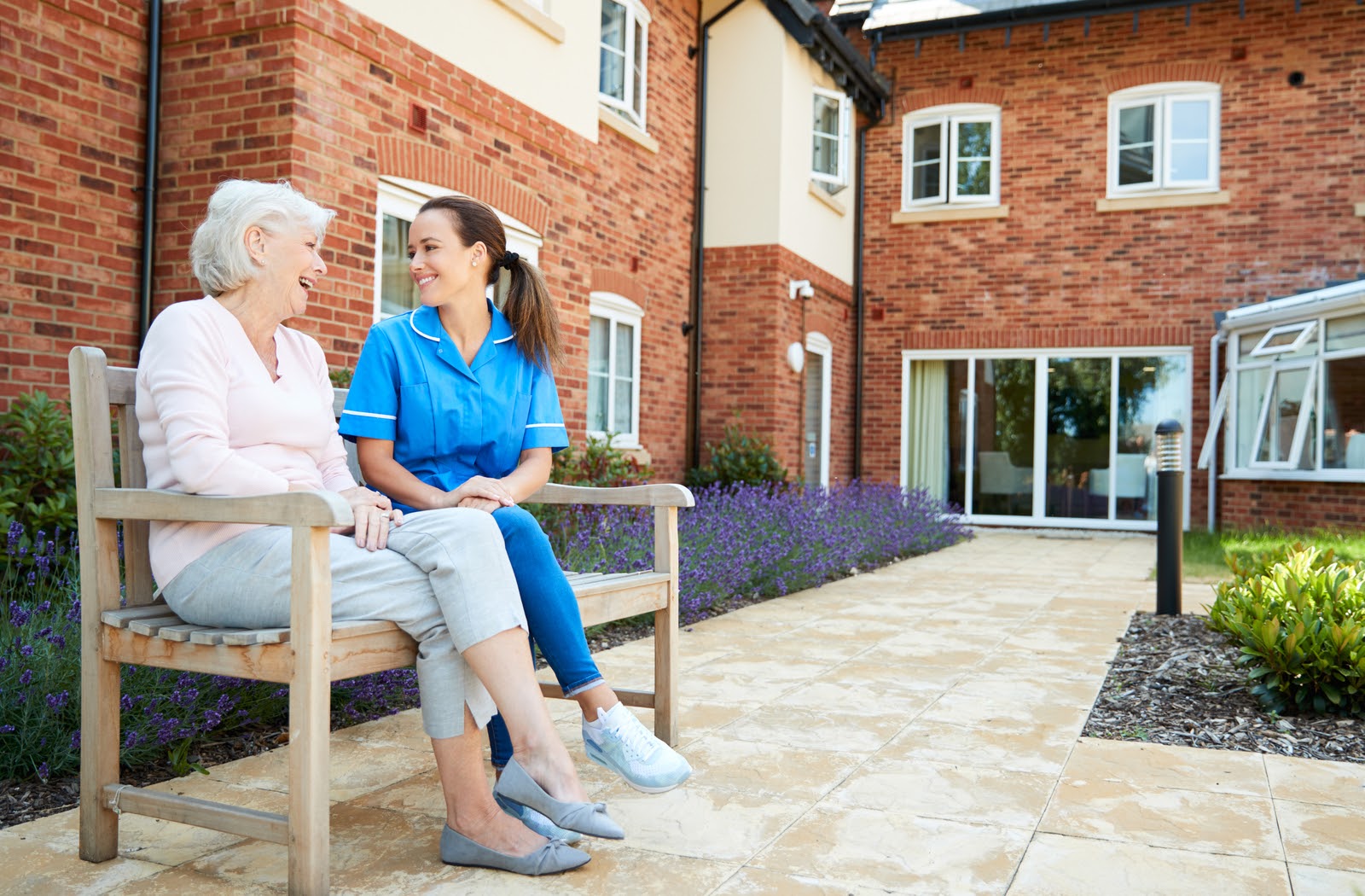 Senior woman sitting on bench outside of apartment talking with nurse.