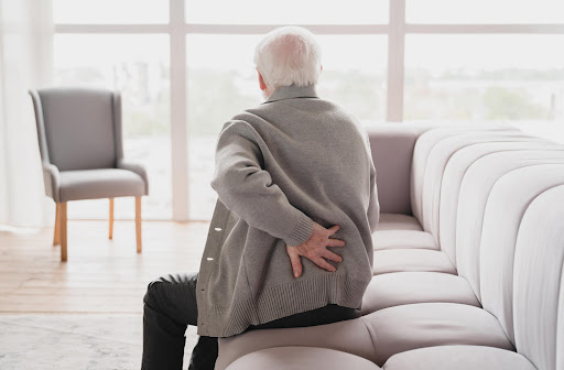 A senior man holds his back in pain while facing away from the camera.