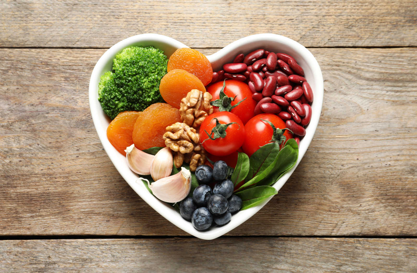 A wooden table with a bowl of various fresh fruits and vegetables, representing a heart-healthy diet.