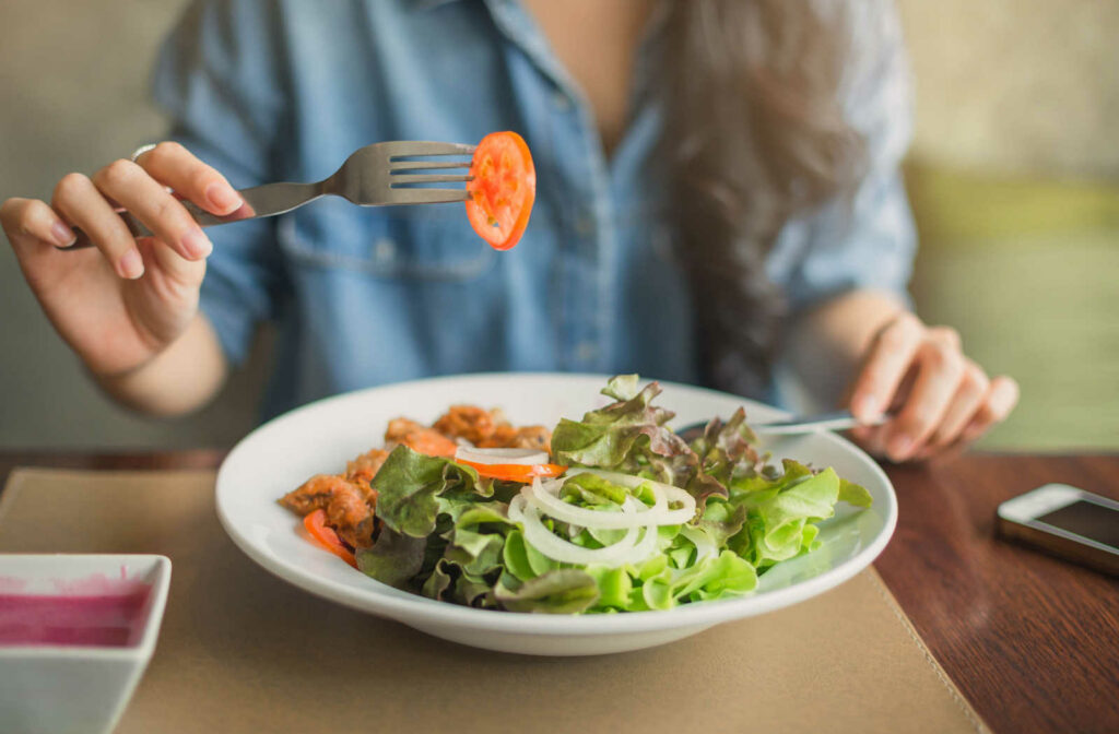 A happy woman sitting at a table and eating a healthy salad, with a smile on her face.