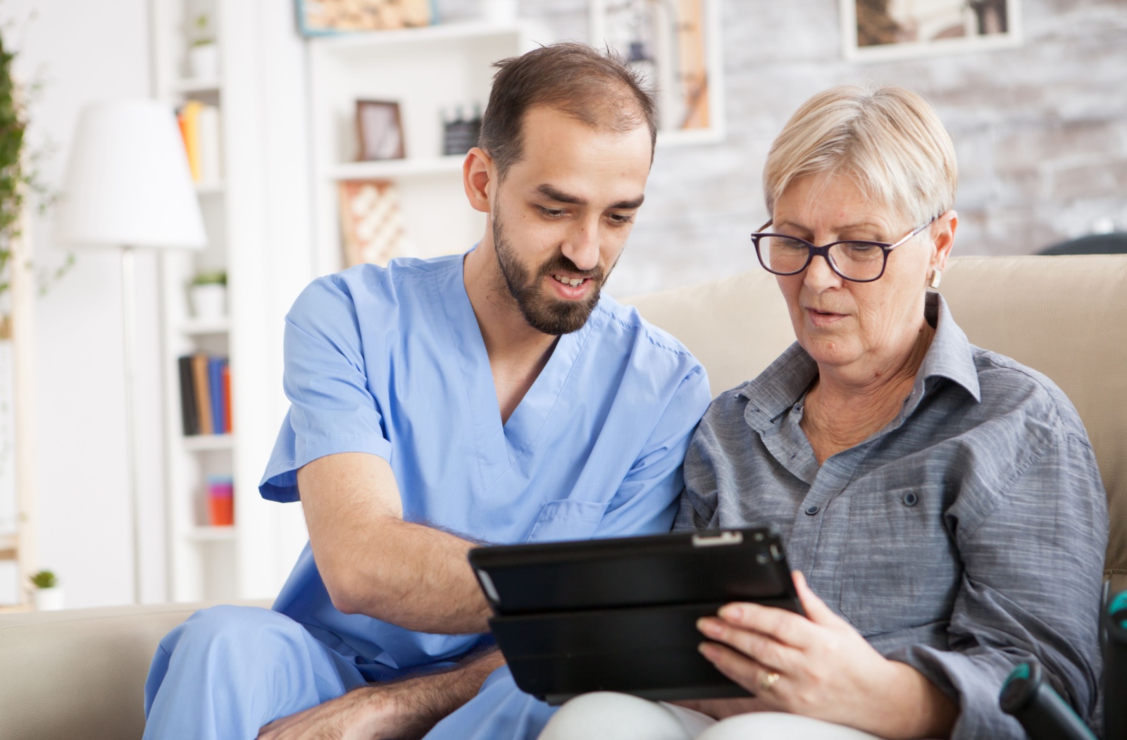 A respite caretaker helping an older adult woman use her tablet.