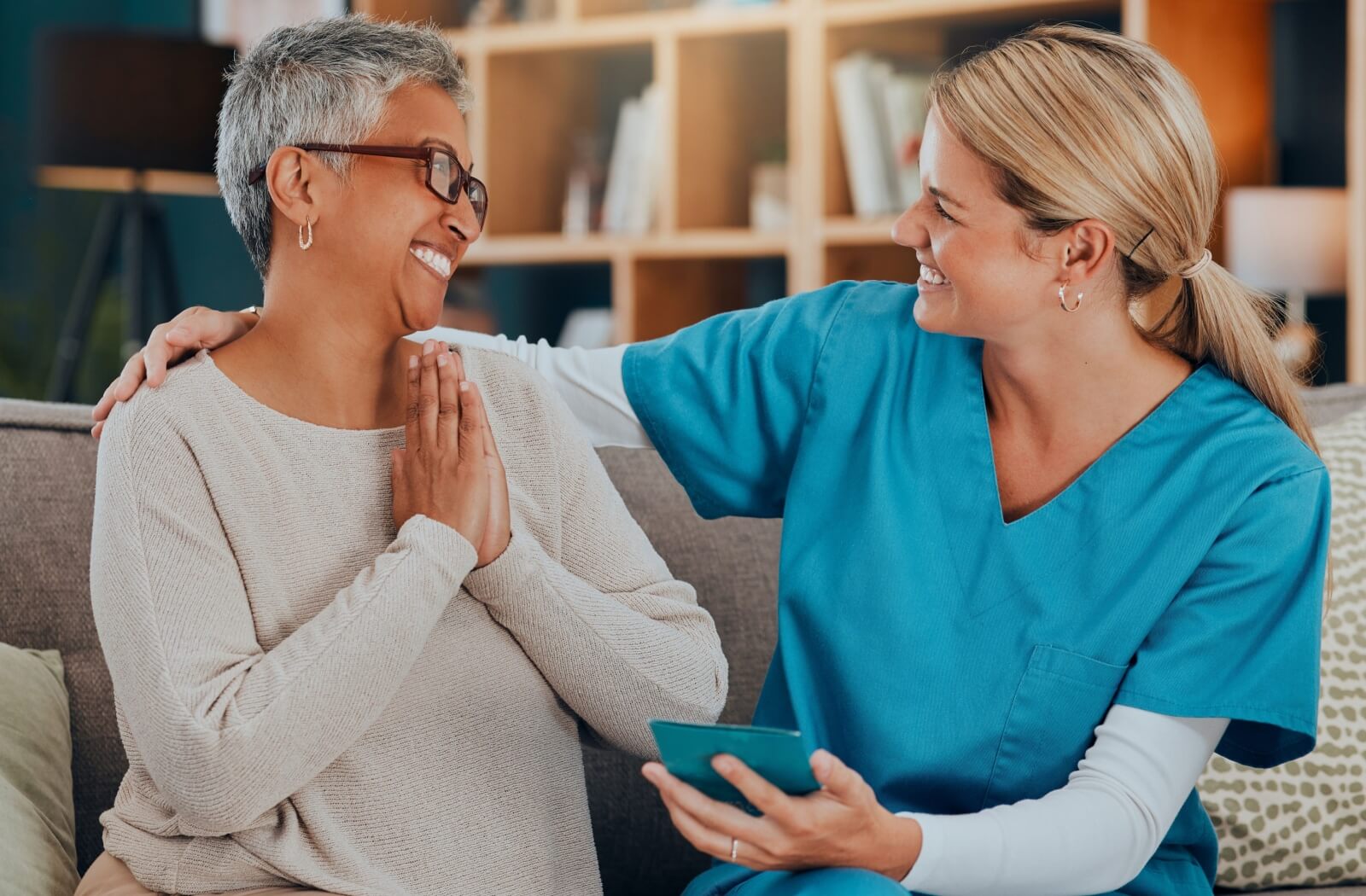 A senior woman and a caregiver sitting on a couch smiling at each other in respite care.