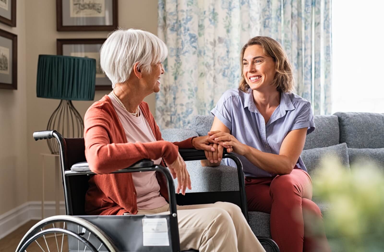 An adult child visiting her older mother after transitioning to memory care, holding her hand and smiling.