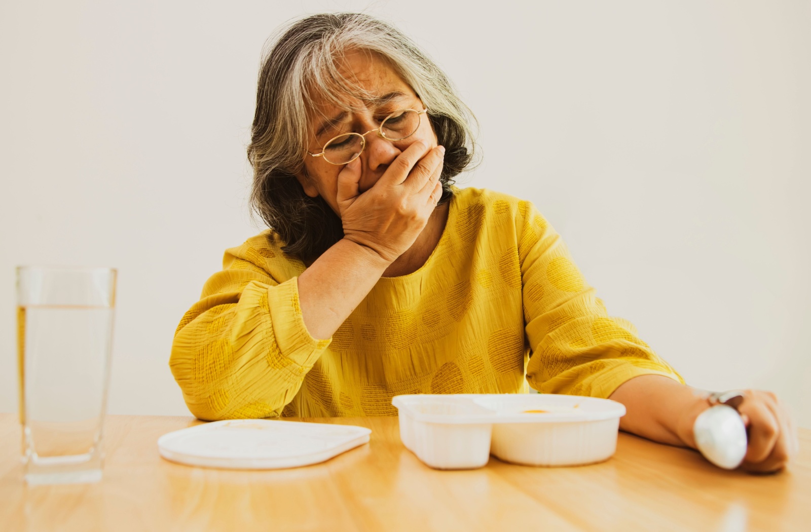 Woman covering her mouth while looking at unappetizing take out container.