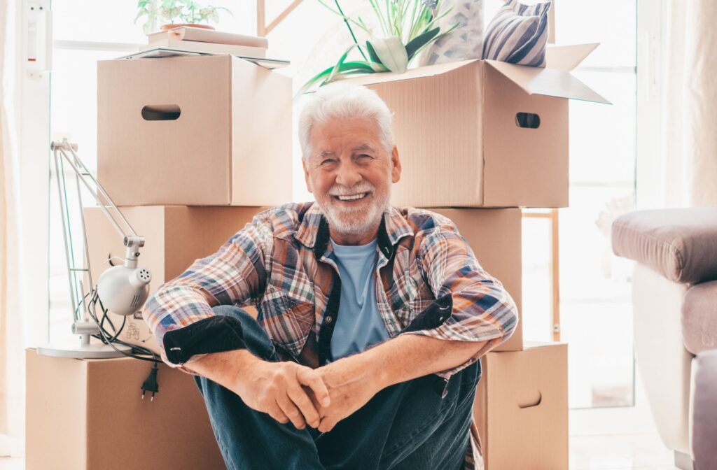 An older man sitting in front of cardboard boxes, smiling warmly, with a sense of contentment and accomplishment.