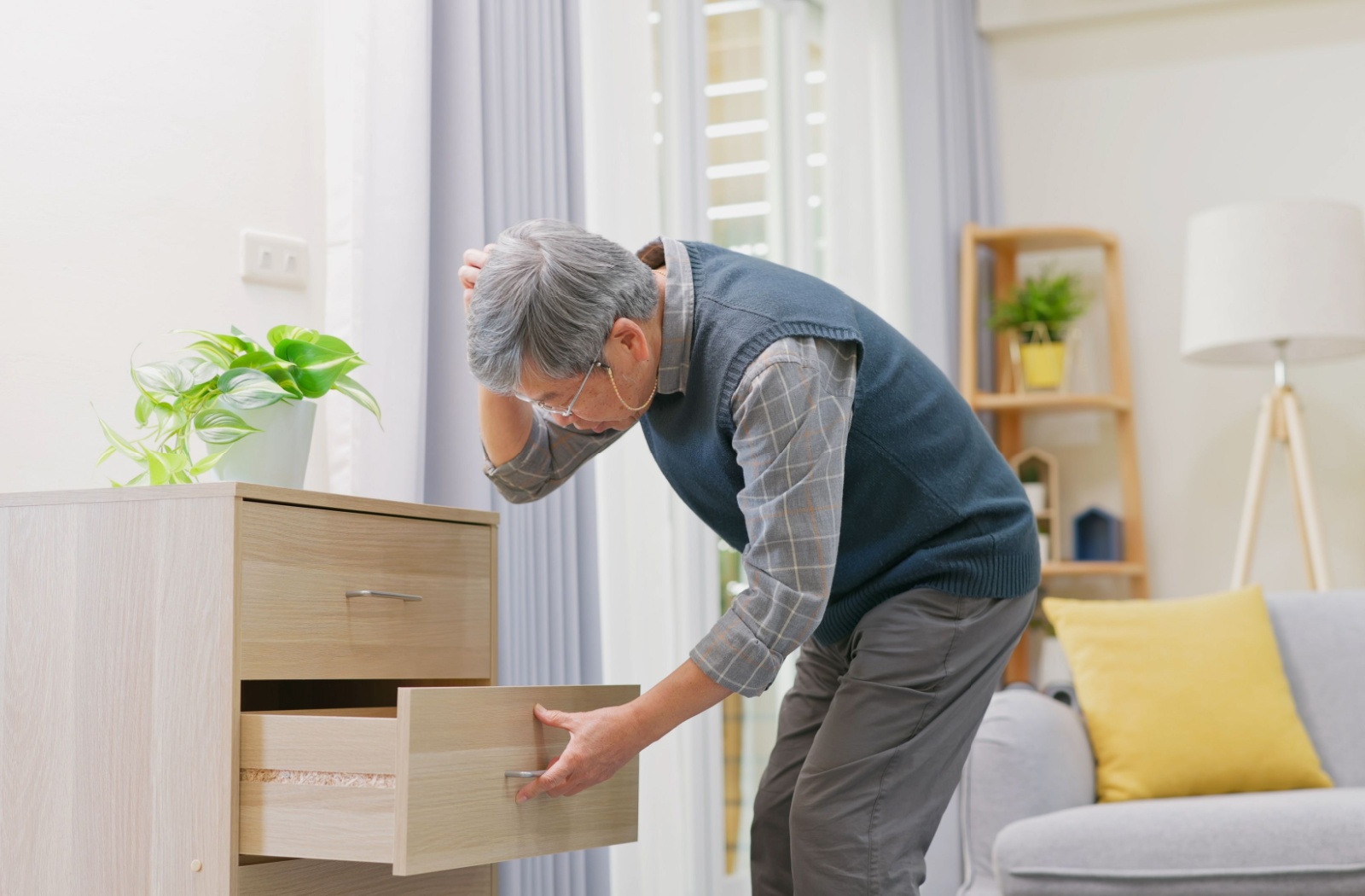 An older man looking into a drawer, appearing confused, in a home setting.