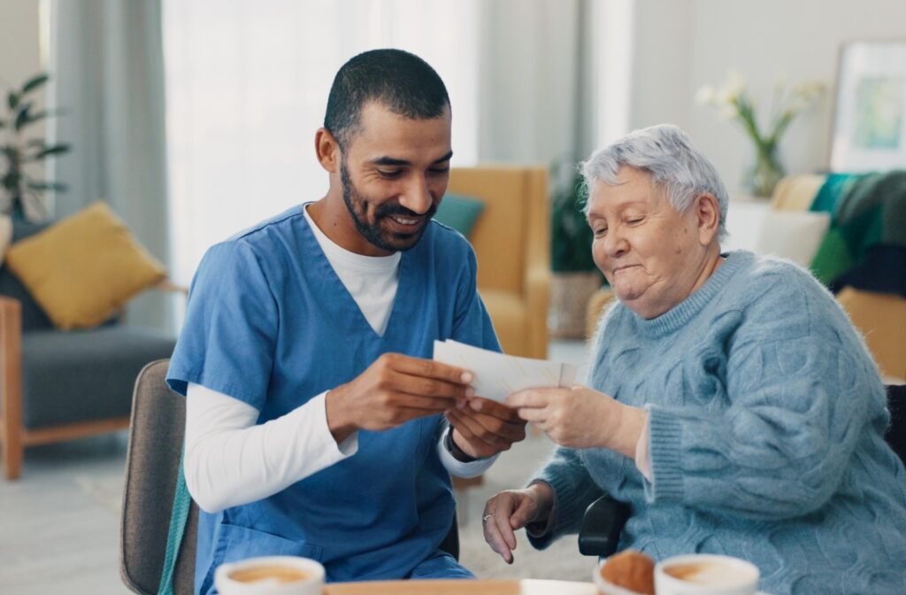A caregiver in scrubs smiling and sharing a photo with an elderly woman during a friendly conversation.